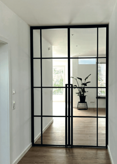 Helle Stahl-Glas-Drehtür mit schwarzem Rahmen als Durchgang zum Wohnbereich