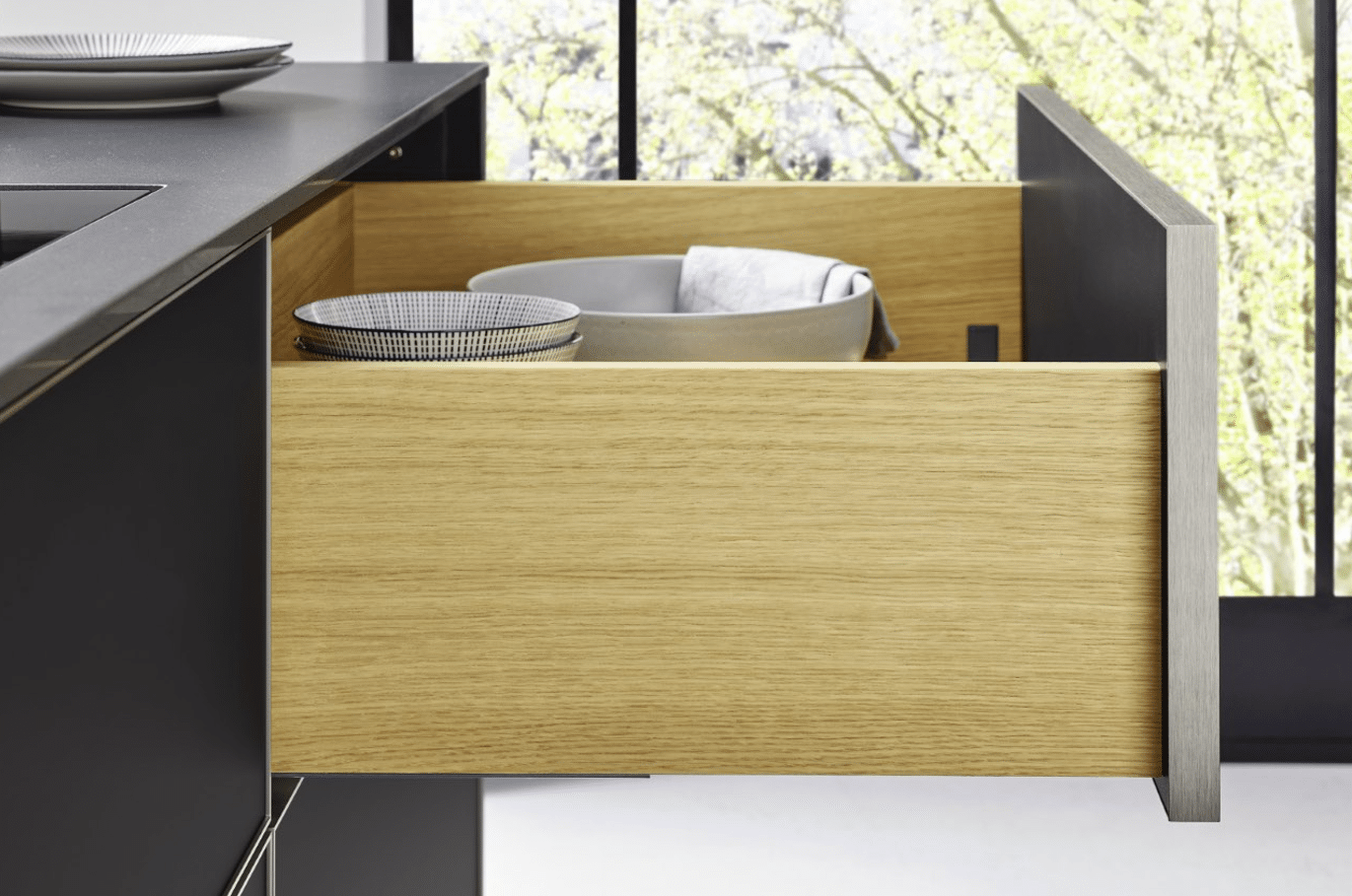 Offene Küchenschublade mit gelbem Holzeinsatz und weißem Geschirr