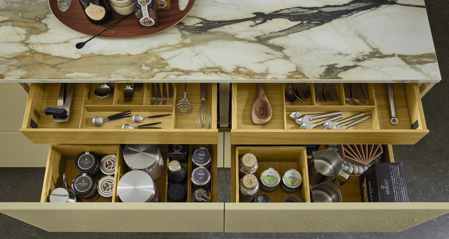 Geöffnete Küchenschubladen mit gelben Einsätzen, Besteck und Geschirr unter Marmorarbeitsplatte